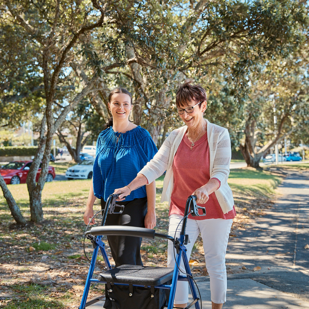 Two women walking in park with one women walking with her AML Four Wheeled 7.3" Castors Rollator
