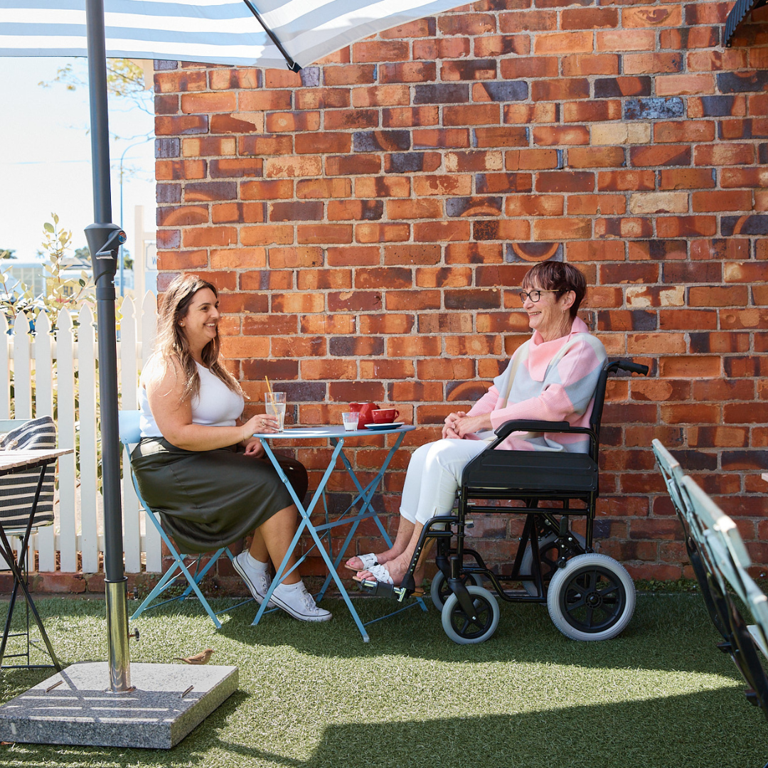 Two women sitting in a cafe. One woman is in a wheelchair from Allied Medical in New Zealand.