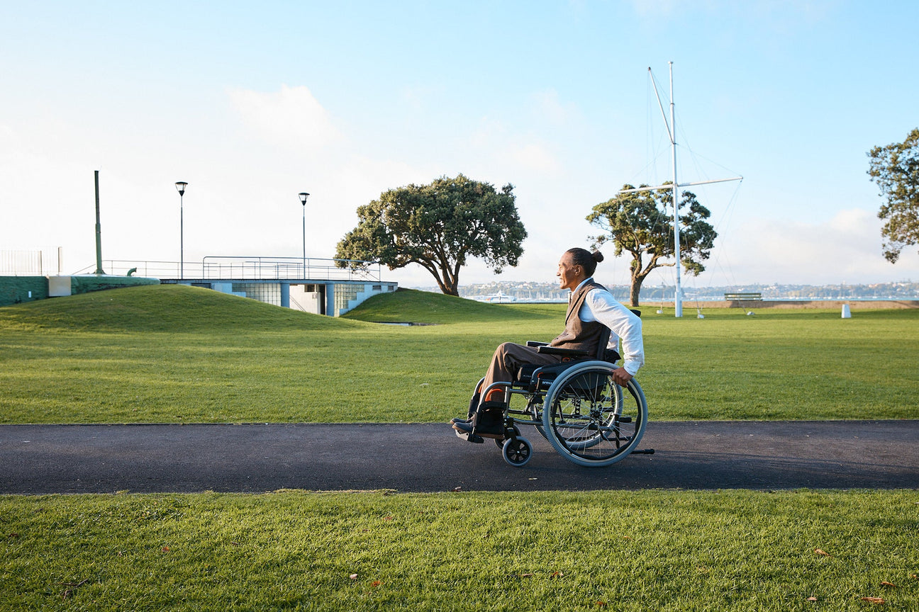 Man in wheelchair on path through a lush green park.