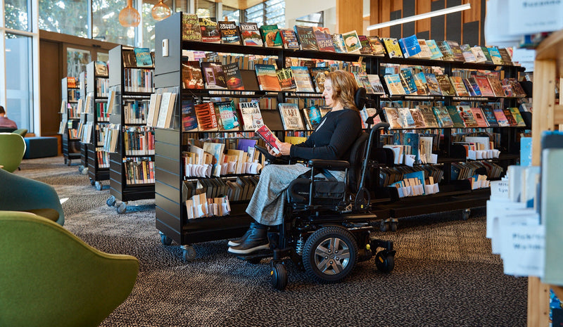 Woman in KP25.2 Powerchair looking at book at the library